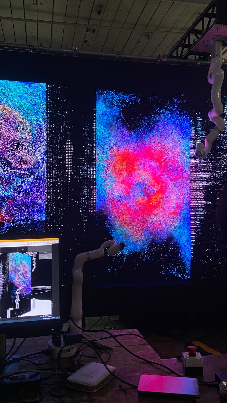 An arm reaching into a dense blue and magenta particle field on the studio LED wall, with an operator screen showing the same field