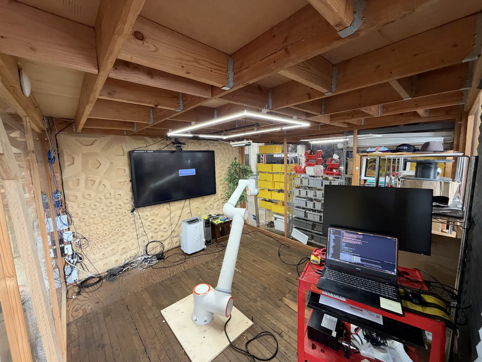A white Fairino FR20 arm on a plywood base in a small lab, with a red cart holding a laptop beside it