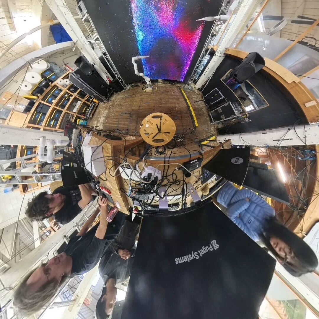 A 360-degree tiny-planet photograph of the studio: the LED wall running particles above, the team standing around the rig below